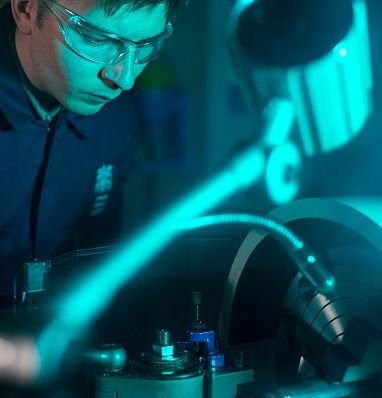 Estudiante con lentes de seguridad opera una máquina iluminada con luz turquesa